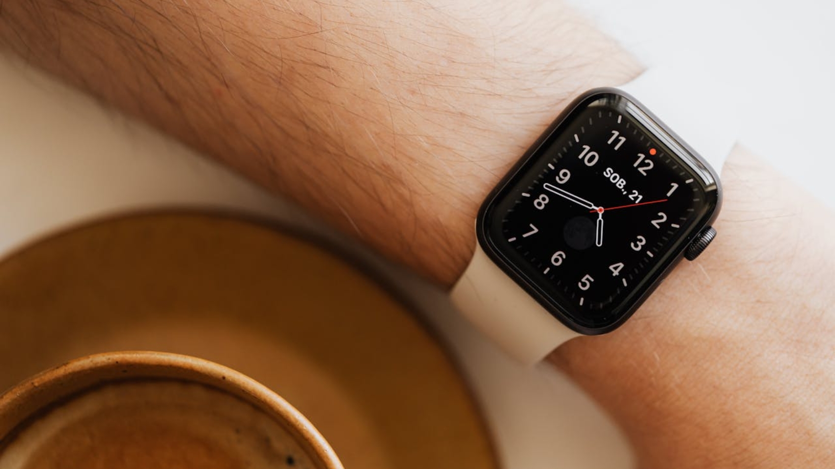 From above closeup of crop man hand with smart watch near cup of hot americano on white background